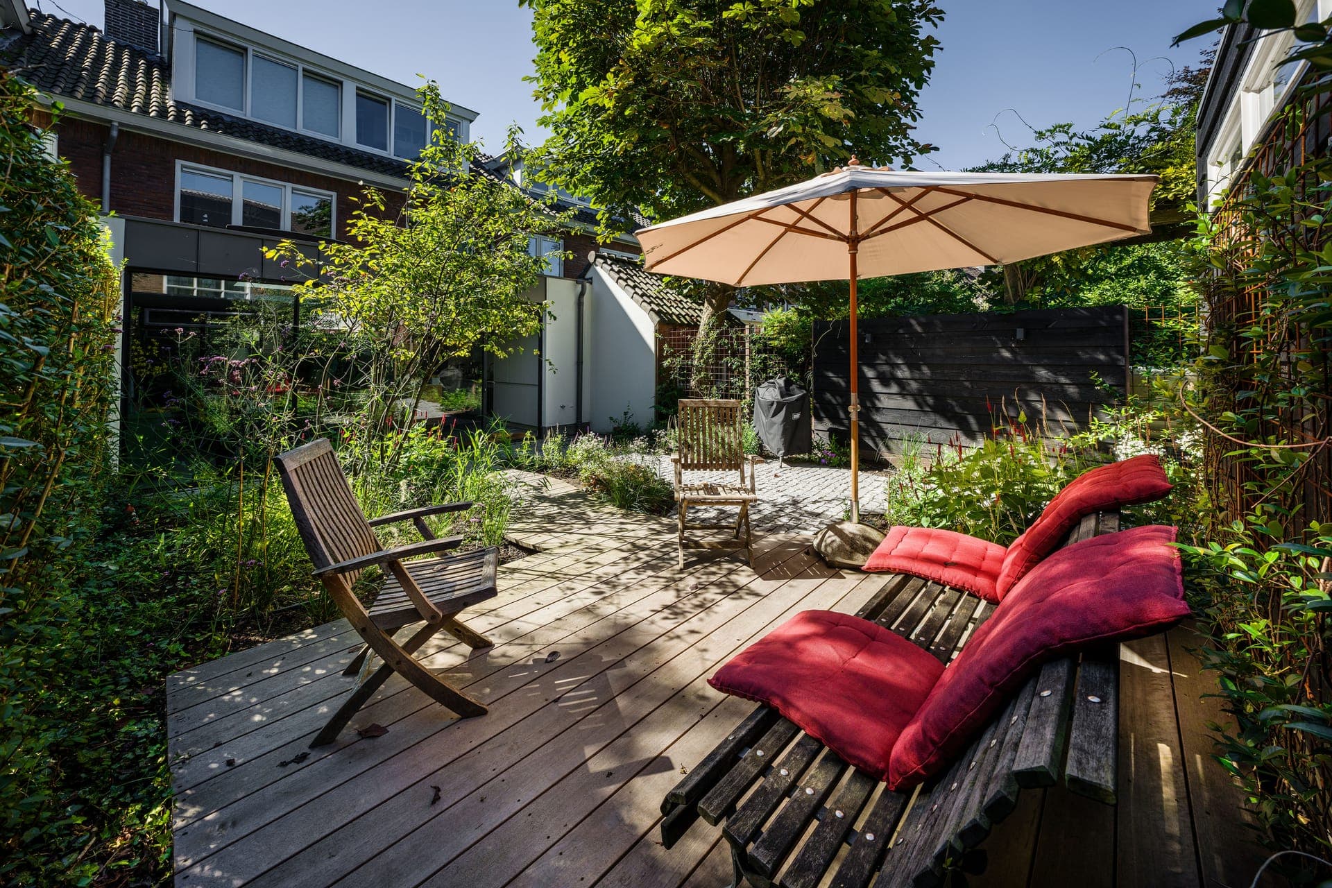 Groene binnentuin met parasol en loungestoelen met rode kussens