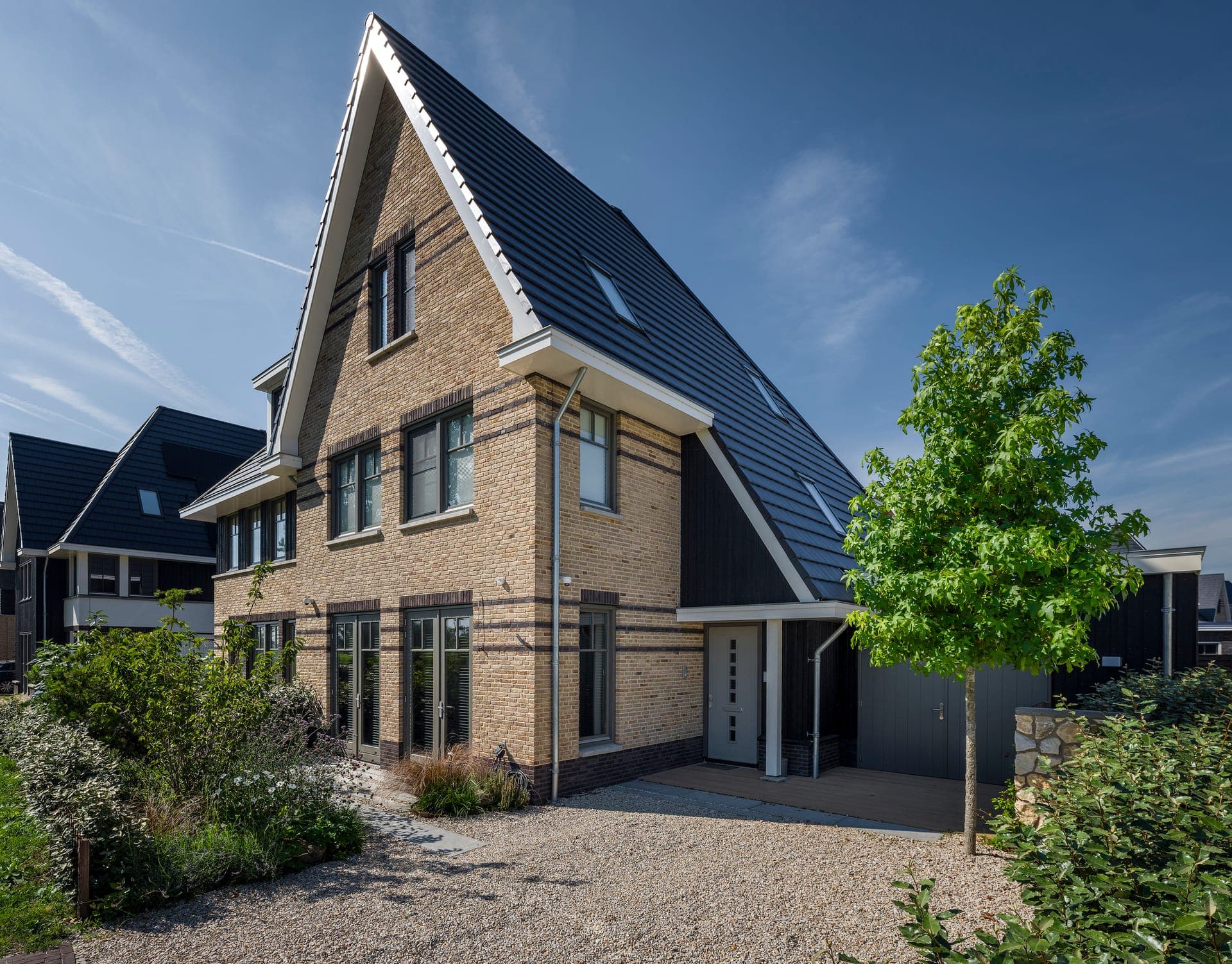 Vooraanzicht van de woning met grindoprit en jonge sierboom