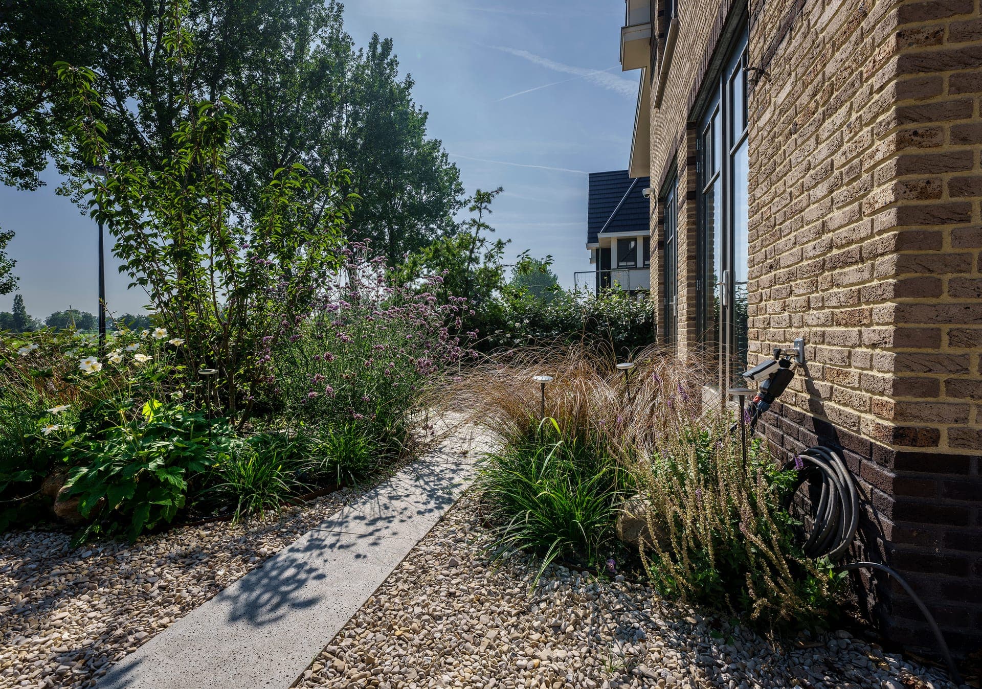 Zijpad langs de woning met grindborder en siergrassen