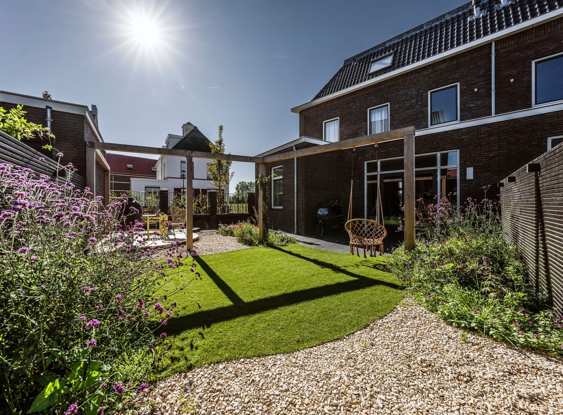 Achtertuin met grindpad, gazon en pergola in tegenlicht