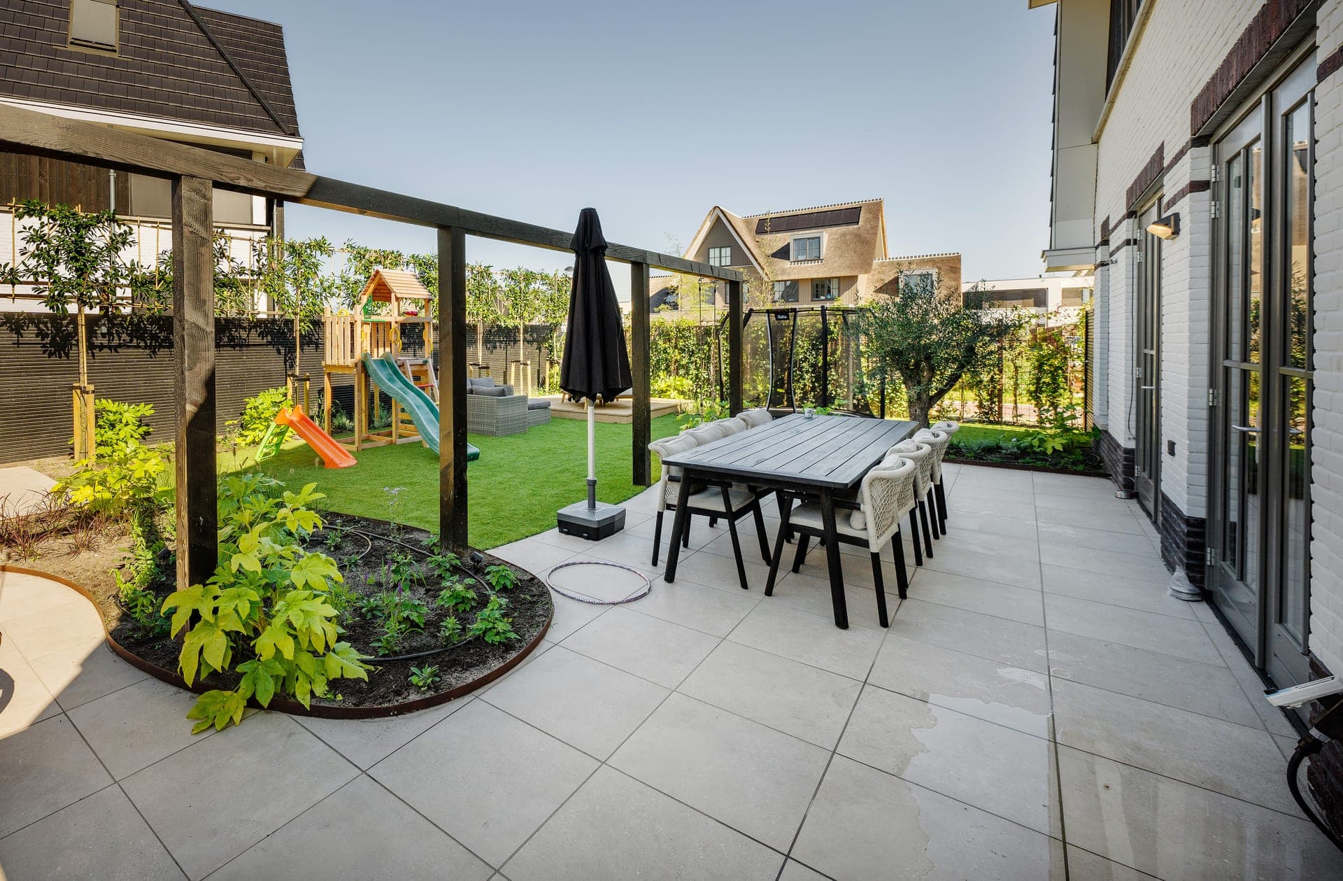 Sfeervol keramisch terras met eettafel, parasol en groene beplanting