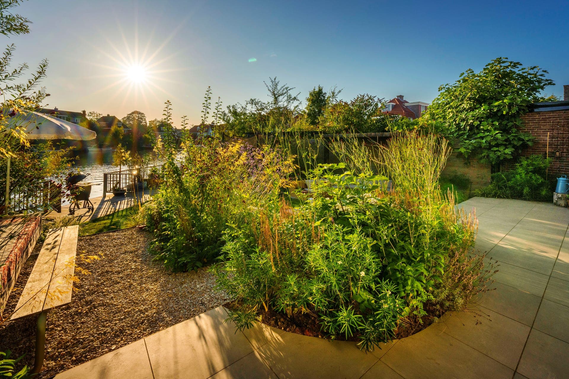 Waterside garden in Overveen built by JLU Tuinen, with borders, gravel and a terrace in the evening sun