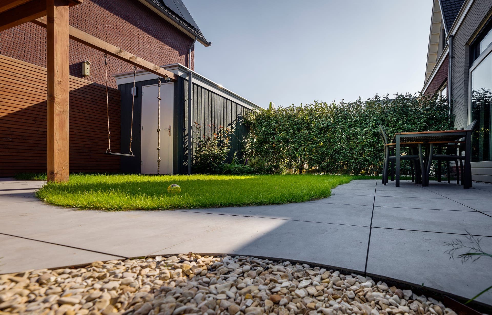 Tuinhuis naast houten overkapping met gazon en grindborder