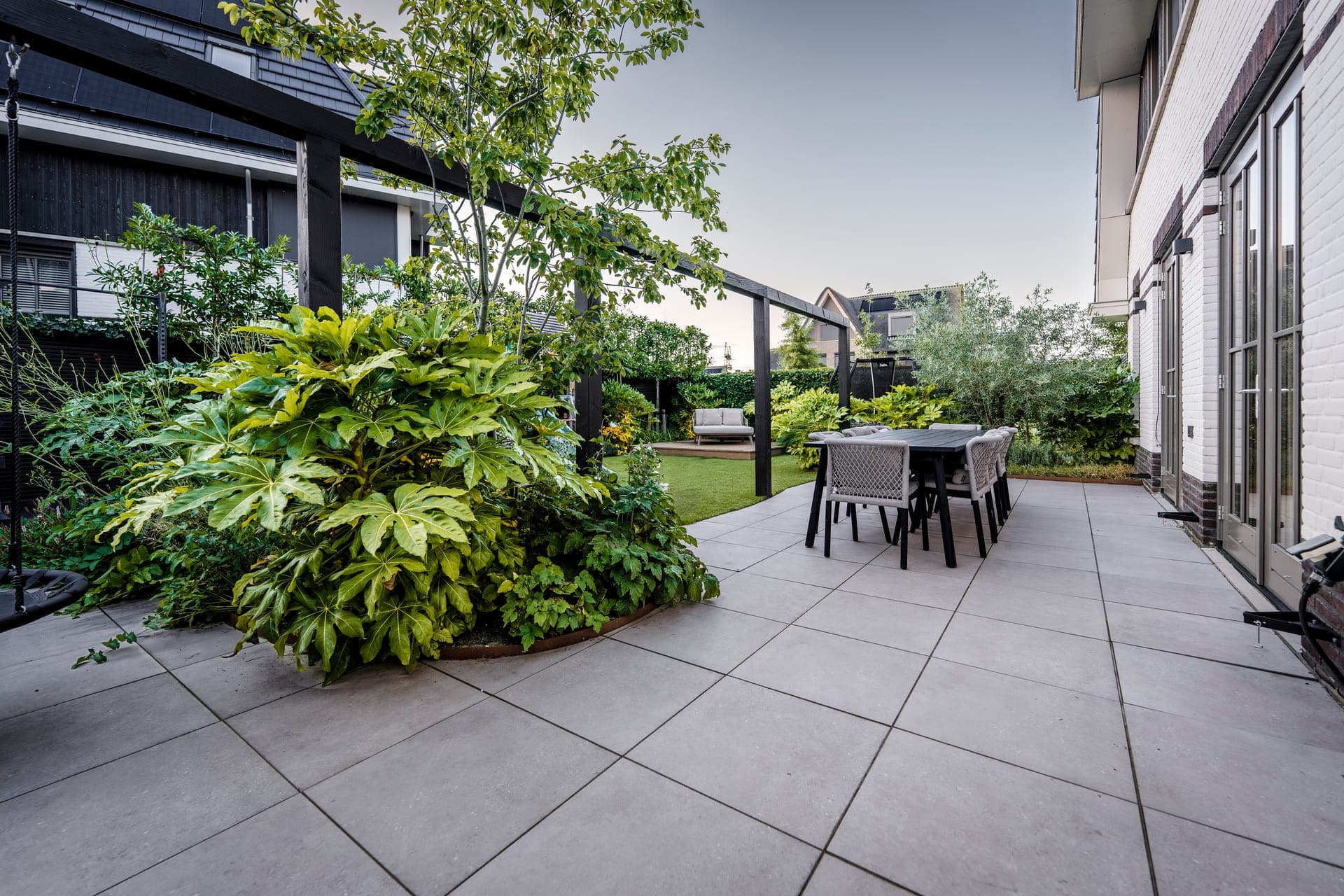 Ruim keramisch tegelterras met eettafel en Fatsia-border in Weesp